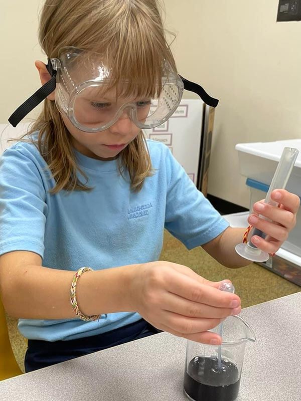 A young female Lahr-Well Academy Student wears protective goggles while doing an experiment in science class.