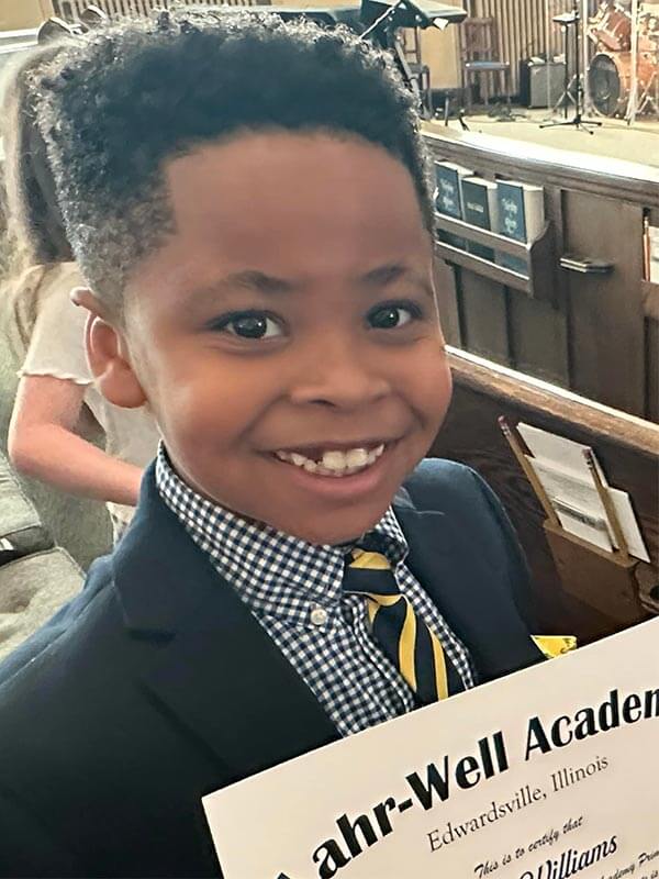 A young male Lahr-Well Academy Student holds up his certificate of grade advancement.