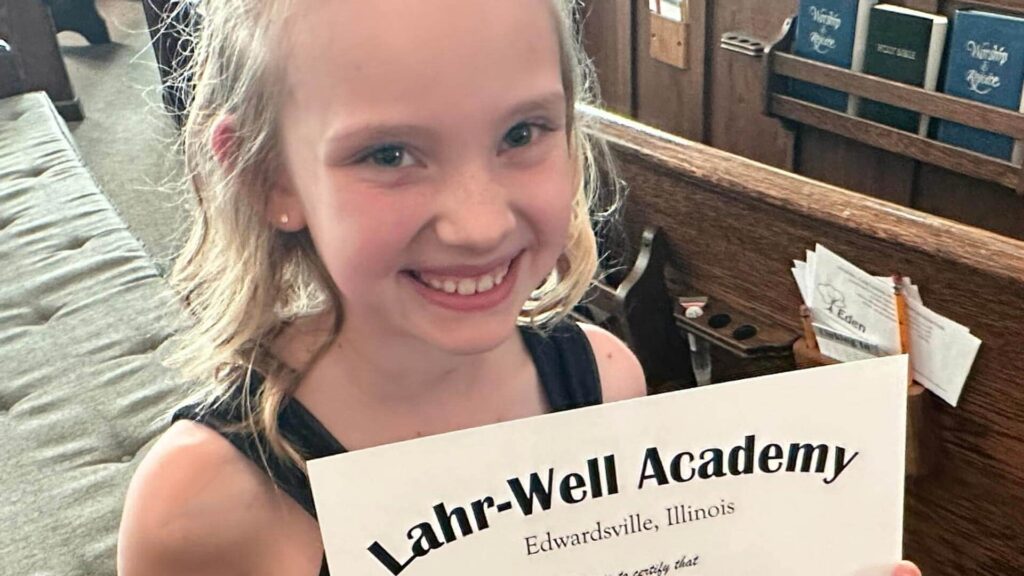 A young female student smiles while holding her certificate of achievement and advancement at a Lahr-Well graduation ceremony.
