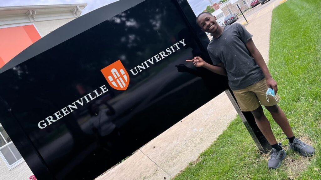 Local Student Prepares for College at Age 15 — Clarence Johnson stands next to the Greenville University sign.